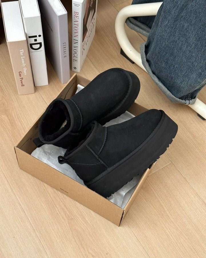 Unboxing moment van de zwarte UGGs in originele verpakking, gefotografeerd boven houten vloer met zicht op binnenvoering