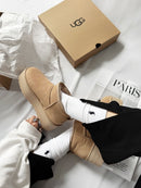 Lifestyle flatlay van de Mustard Seed platform boots naast een open UGG-doos op een wit laken, met kledingaccessoires als stylingdetails