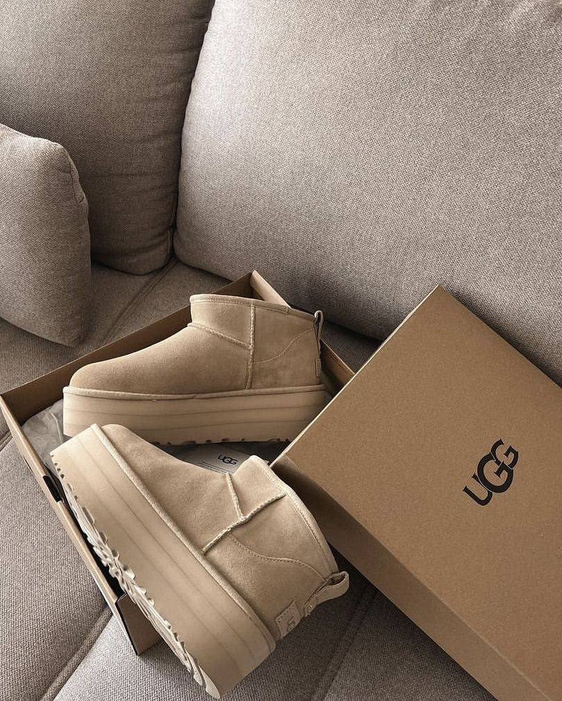 Beige UGG's op zachte bank met UGG-doos op de achtergrond, minimalistisch gefotografeerd in natuurlijke lichtinval voor warm effect