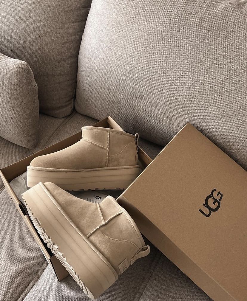Beige UGG's op zachte bank met UGG-doos op de achtergrond, minimalistisch gefotografeerd in natuurlijke lichtinval voor warm effect