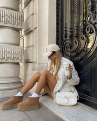 On-feet shot van beige UGG platform boots gedragen met witte sokken op een marmeren traptrede, urban maar cozy vibe