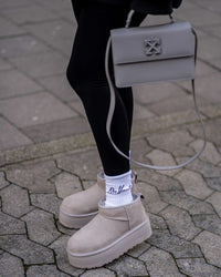Straatbeeld met persoon in zwarte broek en UGG Seal Platforms, close-up op voetstap en reflectie op natte stoeptegels