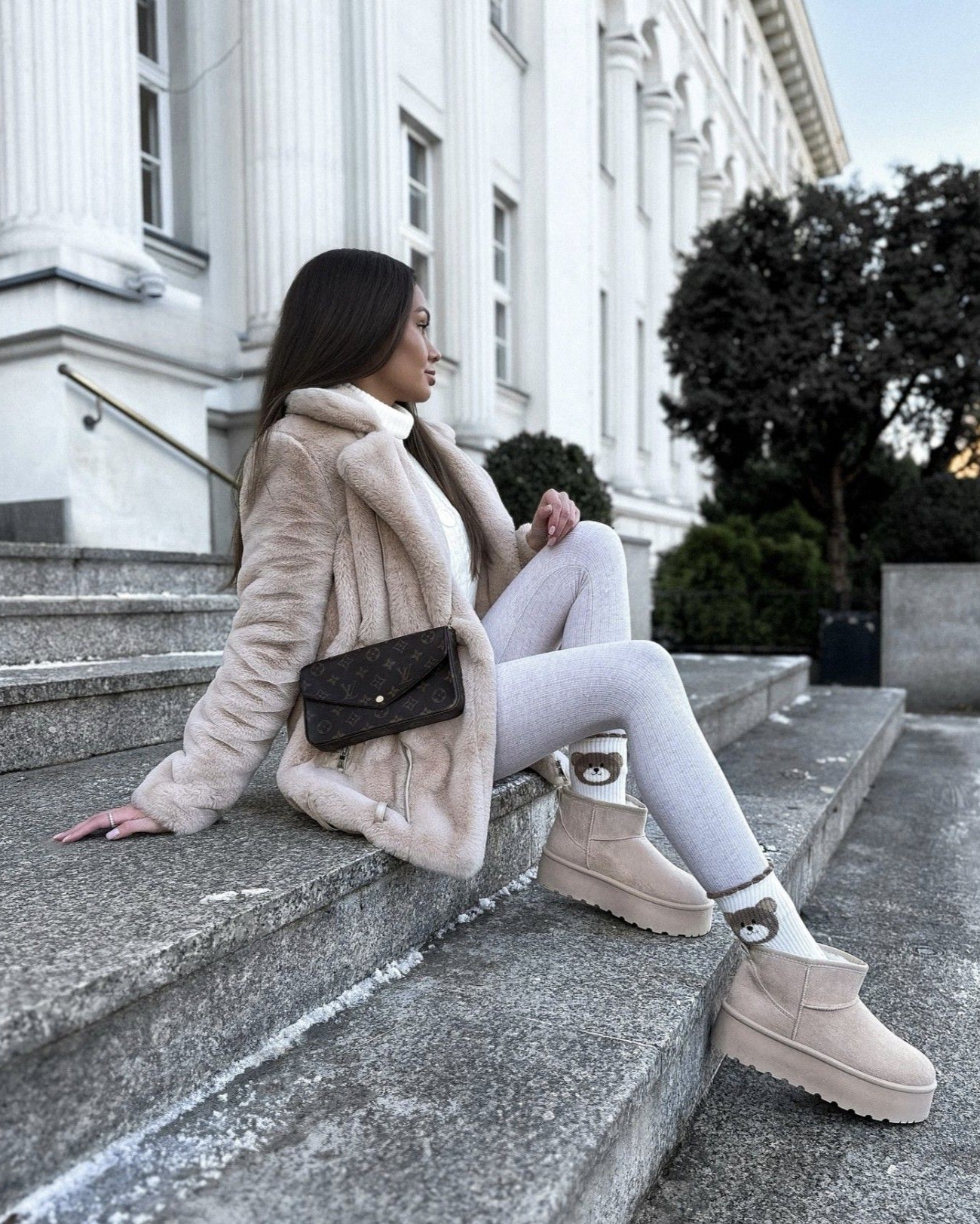 Lifestyle opname van model op marmeren trappen met beige trenchcoat en UGG Classic Seal aan, gefotografeerd in stedelijke omgeving