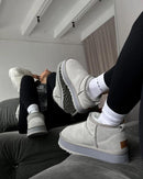 Cozy indoor moment met witte sokken in de Seal grey UGGs op zachte vloer, benen omhoog tegen witte muur in clean interieur