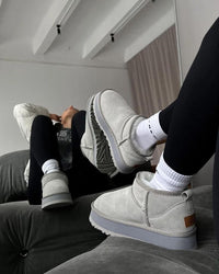 Cozy indoor moment met witte sokken in de Seal grey UGGs op zachte vloer, benen omhoog tegen witte muur in clean interieur