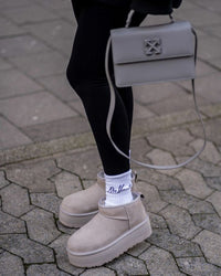 Straatbeeld met persoon in zwarte broek en UGG Seal Platforms, close-up op voetstap en reflectie op natte stoeptegels