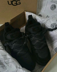 Unboxing van de UGG Lowmel Black met zichtbare doos en beschermpapier, scherp gefocust op het suède materiaal