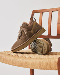 UGG Lowmel Hickory casual gepositioneerd op houten stoel met bol garen, toont lifestyle sfeer en materialen van dichtbij