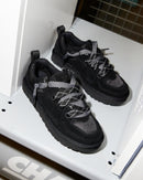 Flatlay van twee zwarte UGG Lowmel Lo sneakers in witte kast, met zicht op veters, suède textuur en rubberen zool