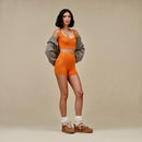Volledige outfitfoto met model in oranje set en UGG Lowmel Lo Chestnut aan, geposeerd in neutrale studio met beige achtergrond