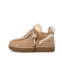 Zijkant van de UGG Lowmel Sand voor kinderen, beige upper met shearling tong en robuuste bruine zool tegen witte achtergrond