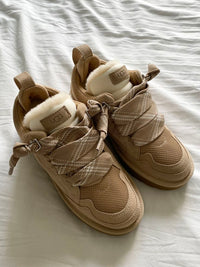 UGG Lowmel kinderschoenen casual neergelegd op beddengoed, met zicht op zachte binnenvoering en vetersluiting