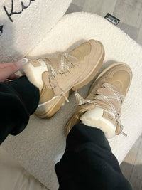 Kindervoeten in de beige Lowmel Sand sneakers, gecombineerd met zwarte joggers en witte vloer in ochtendlicht