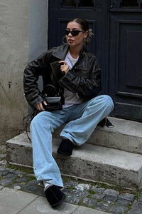 Detailopname van het UGG-logo op de zwarte suède buitenzijde, met zichtbare voering en Tasman-stiksel