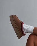 UGG Tazz Slipper Chestnut 1143776K-CHE zijaanzicht met verhoogde platformzool en rode gevlochten rand, gefotografeerd tegen een neutrale achtergrond door Snrkickz.