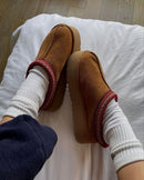 UGG Tazz Slipper Chestnut 1143776K-CHE gedragen on-feet met sokken, warme chestnut suède slipper en rode braid kraag zichtbaar in cozy indoor setting, vastgelegd door Snrkickz.